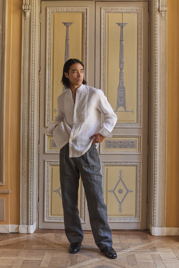 Homme portant la chemise blanche COMÉDIEN en lin avec un plastron plissé, et le pantalon HORIZON en lin plâtré gris anthracite dans l'Hôtel de Bourrienne, plan plein pied.