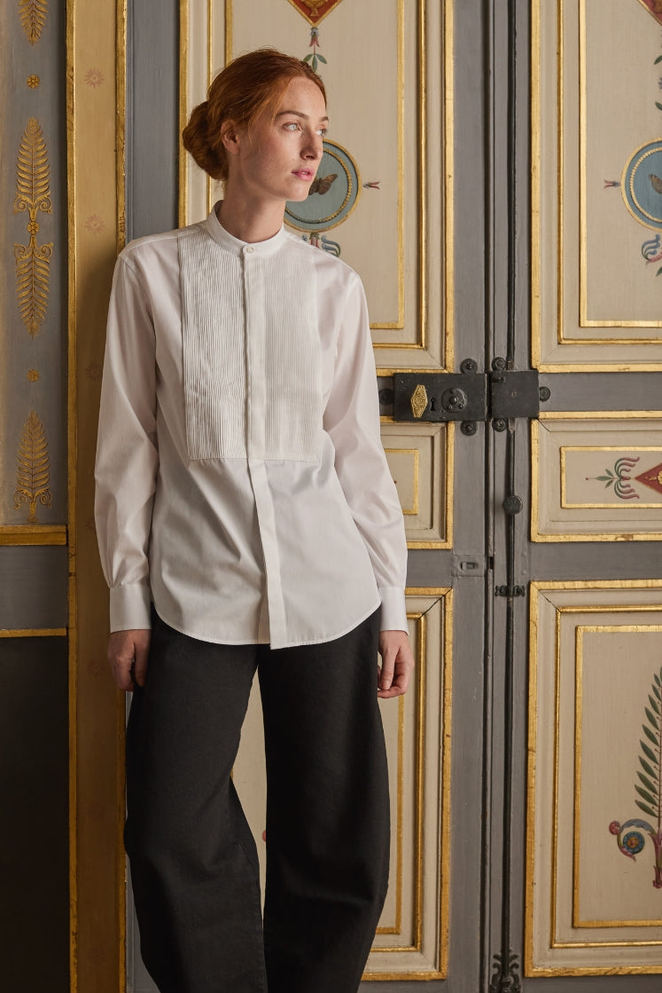 Femme portant la chemise COMÉDIENNE à plastron plissé et col officier, associée à un pantalon noir.