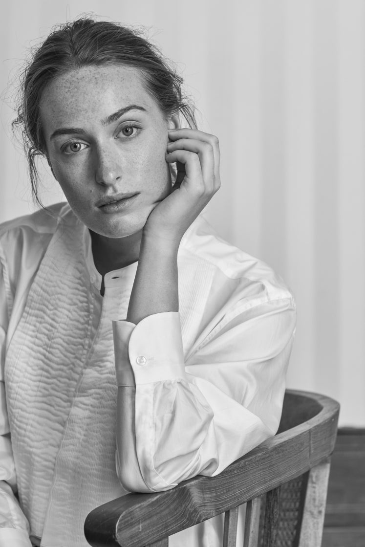 Femme assise sur une chaise portant la chemise COMÉDIENNE à plastron plissé.