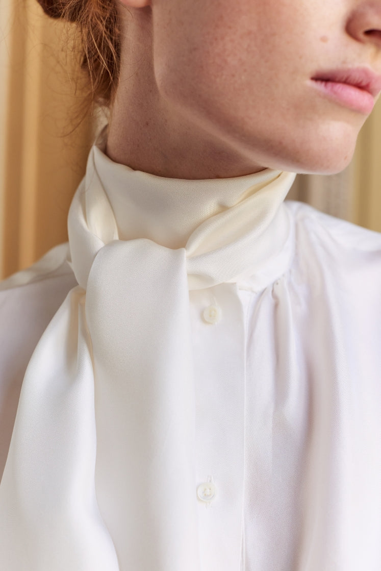 Femme portant la chemise blanche COMTESSE en soie avec un col lavallière noué.