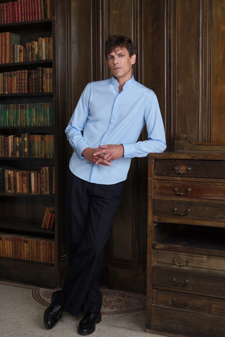 Homme dans une bibliothèque portant une chemise en coton bleue, col officier.