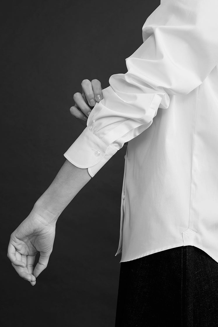 Close-up sur la manche de la chemise blanche intemporelle, légèrement retroussée, poignet classique.