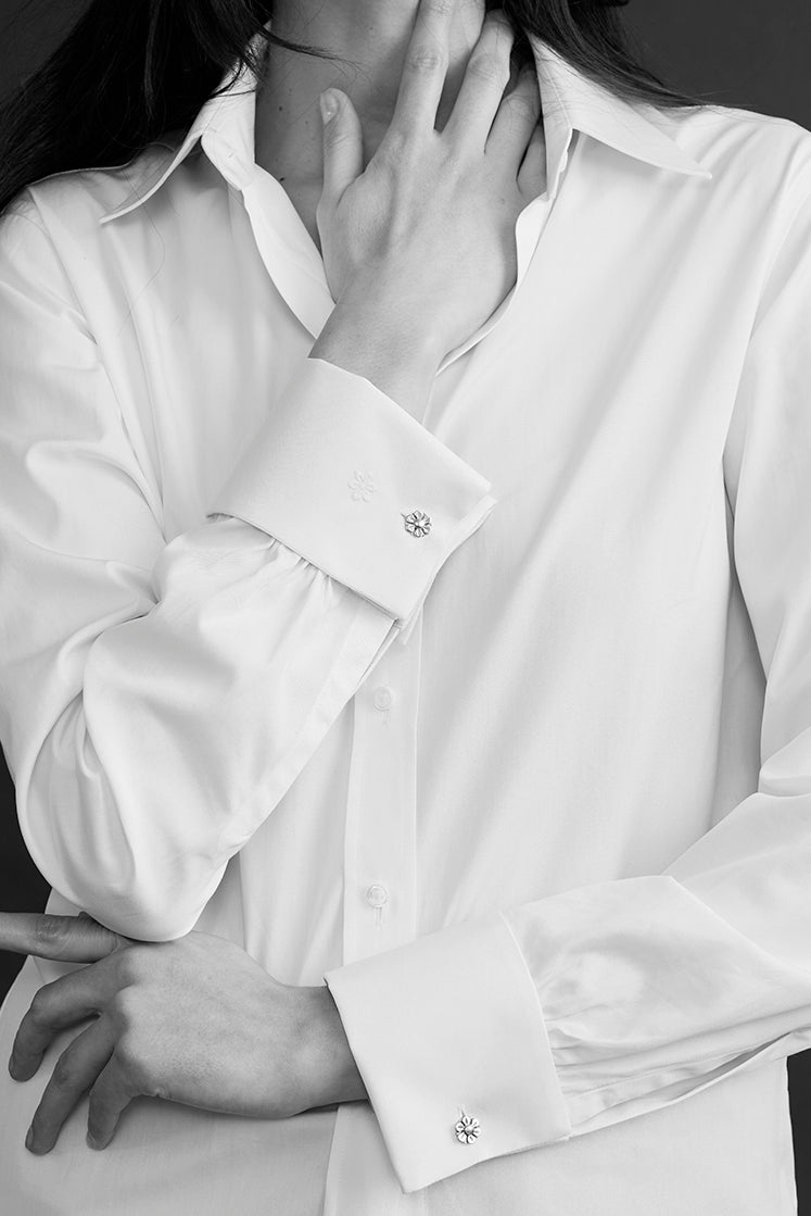 Portrait noir et blanc d’une femme en chemise blanche intemporelle, à col français et poignets mousquetaires avec boutons de manchettes reprenant la Fleur de l'Hôtel de Bourrienne.