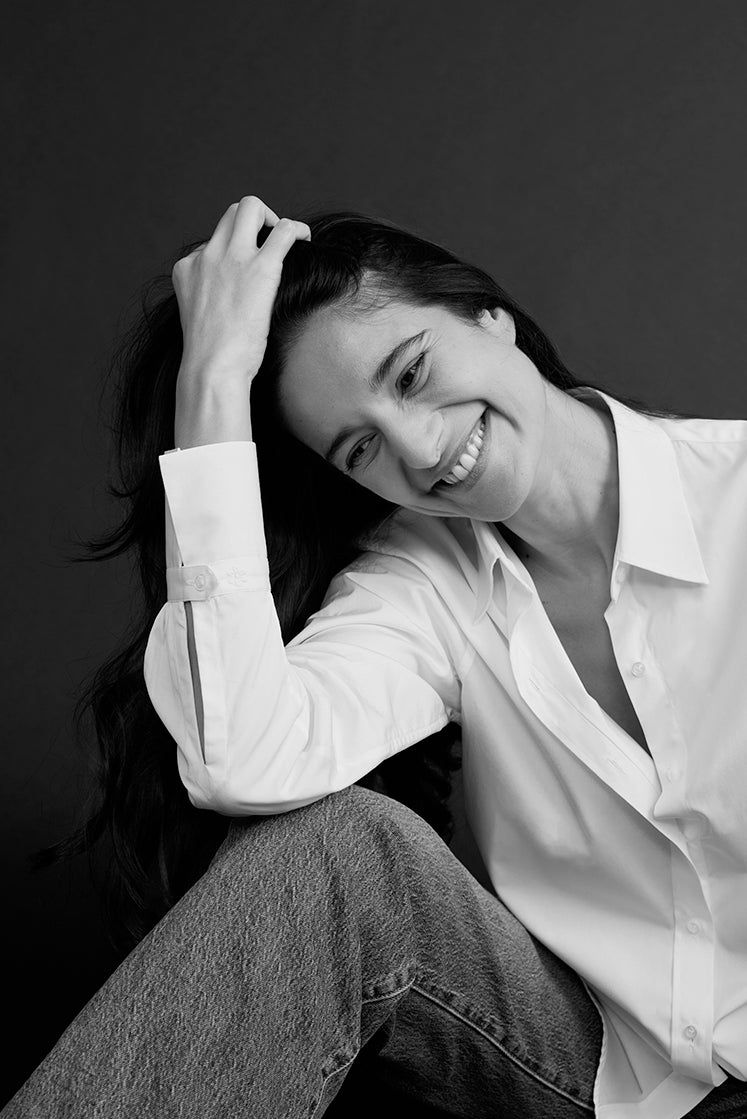 Femme riant, passant sa main dans ses cheveux, portant une chemise blanche élégante, avec un poignet Bourrienne.