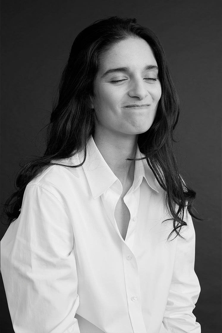 Femme riant portant une chemise blanche élégante, photographiée en noir et blanc, plan buste.