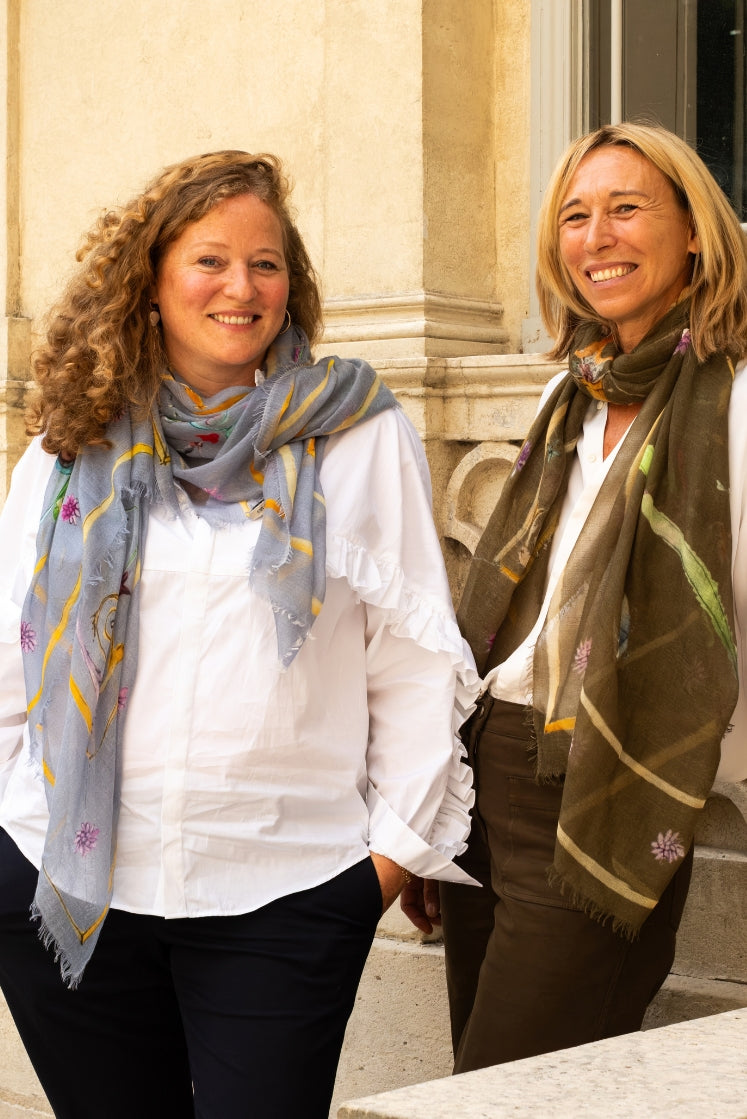 Deux femmes souriantes en chemise blanches portant des Écharpe en cachemire à motifs.