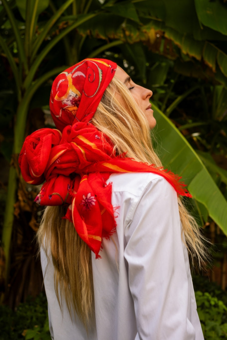 Femme portant l'écharpe Fortunée en cachemire rouge sur la tête dans un jardin.