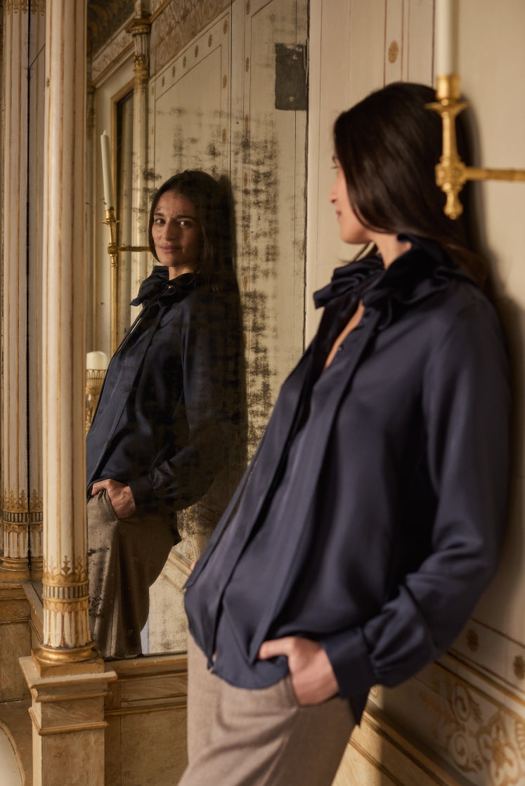 Mannequin adossée contre un mur, regardant son reflet dans un miroir ancien, portant la chemise PASTEL en soie navy, dans un décor historique.