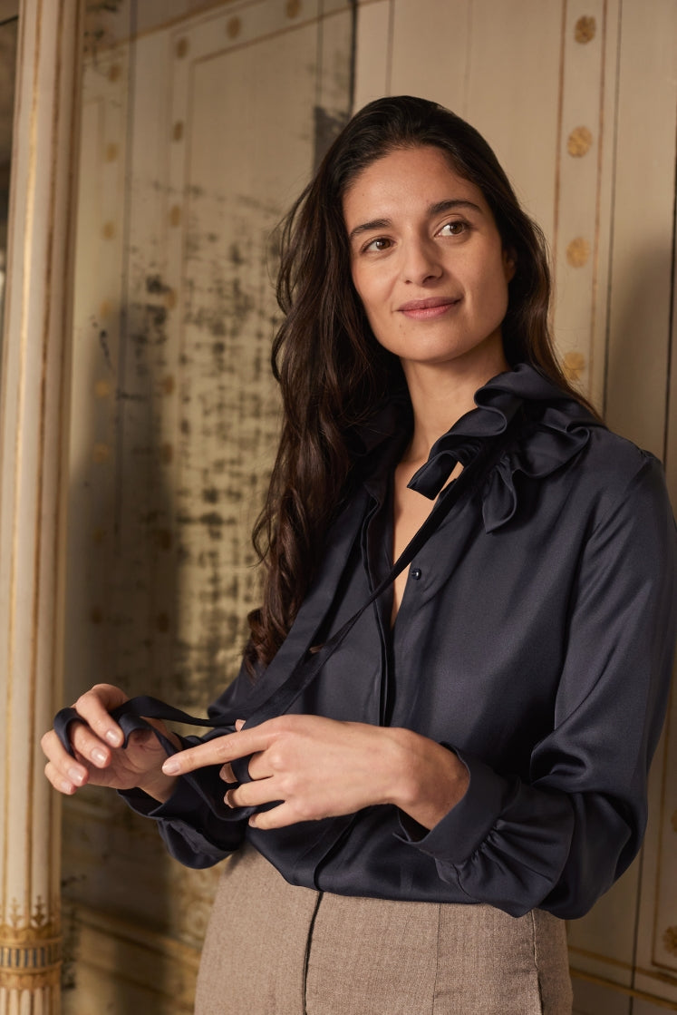 Mannequin portant la chemise PASTEL en soie navy, tenant dans ses mains les liens du col à nouer.