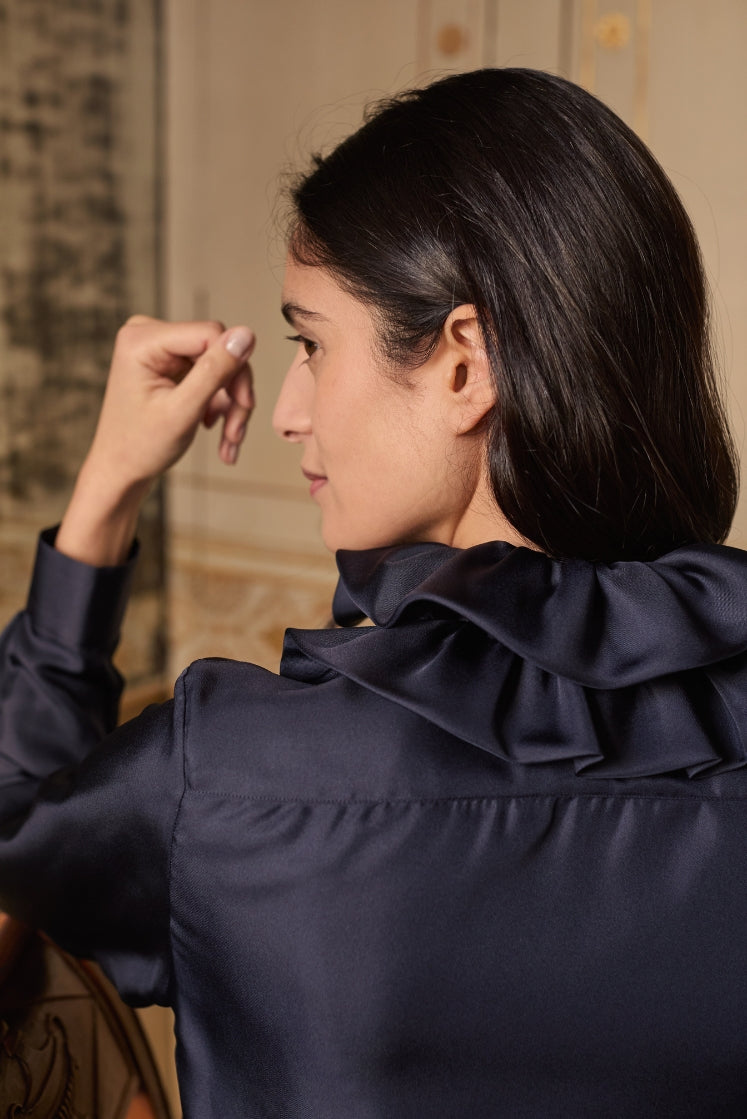 Mannequin assise de dos, portant la chemise PASTEL en soie navy avec son col volanté.