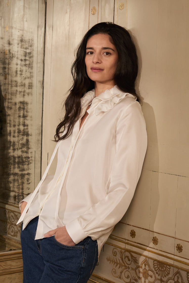Mannequin adossée contre un mur, portant la chemise PASTEL en soie blanche.