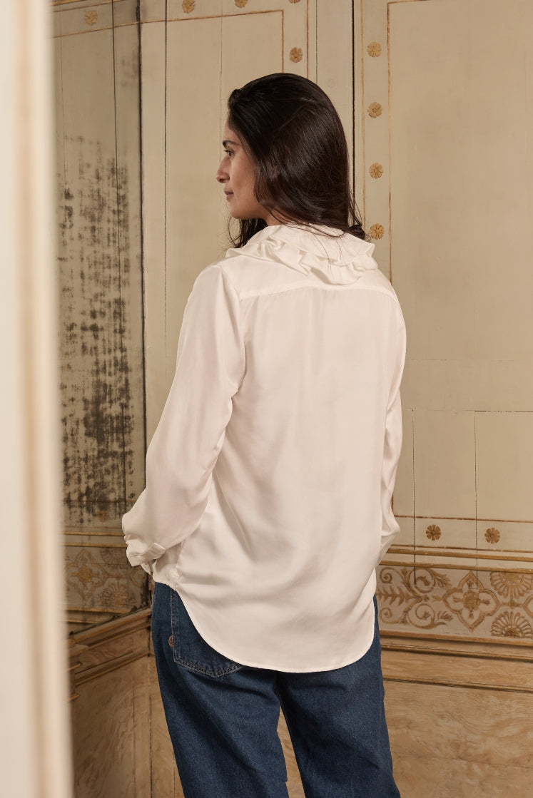 Mannequin portant la chemise PASTEL en soie blanche avec un col à volants, posant de dos dans un décor historique.