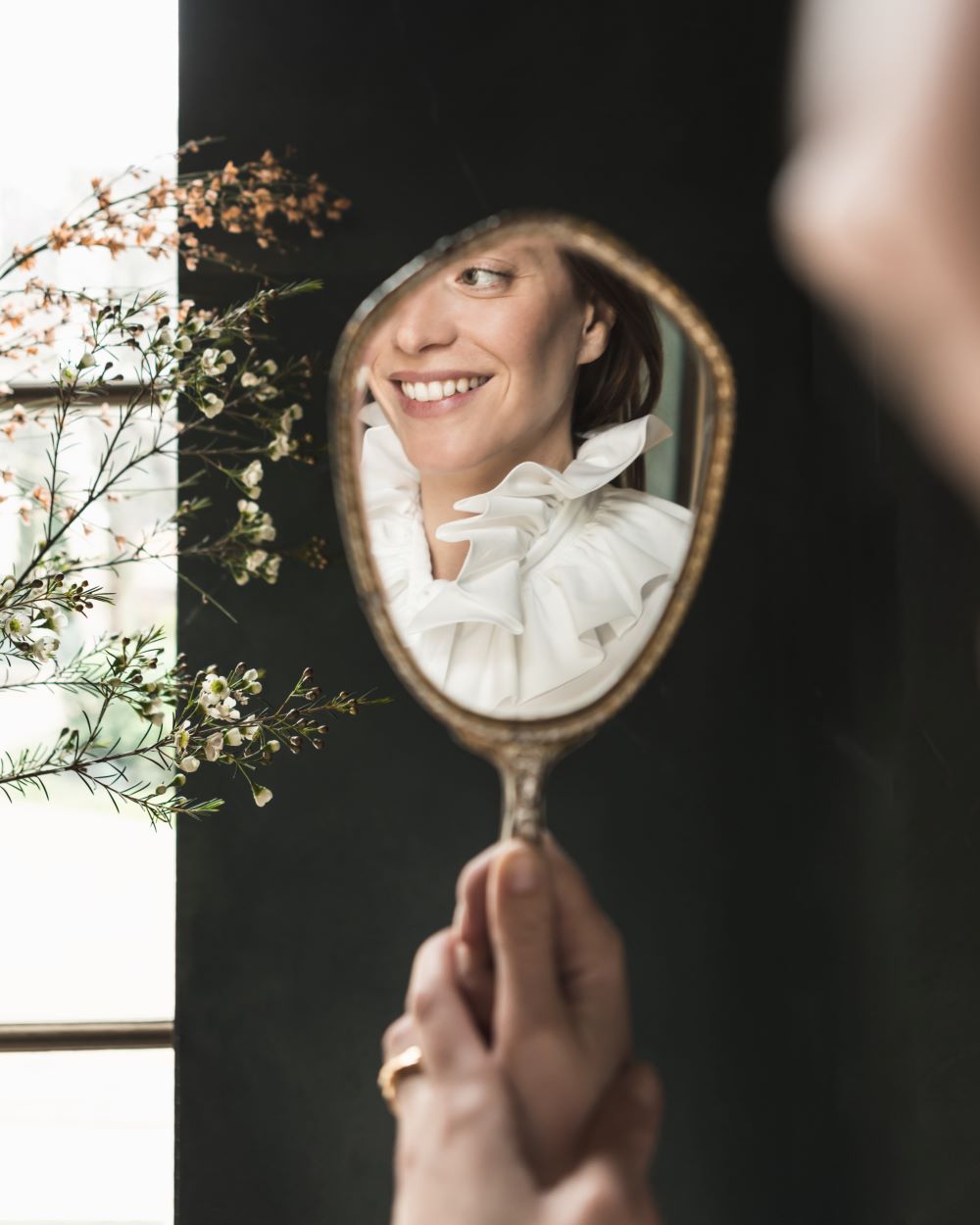 Reflet d'une femme dans un miroir de poche portant la chemise PASTEL avec un col à volants.