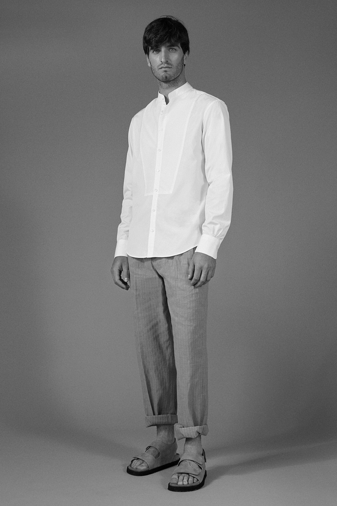 Plan plein pied d'un homme posant en chemise blanche à plastron, avec un col officier et des poignets classiques.