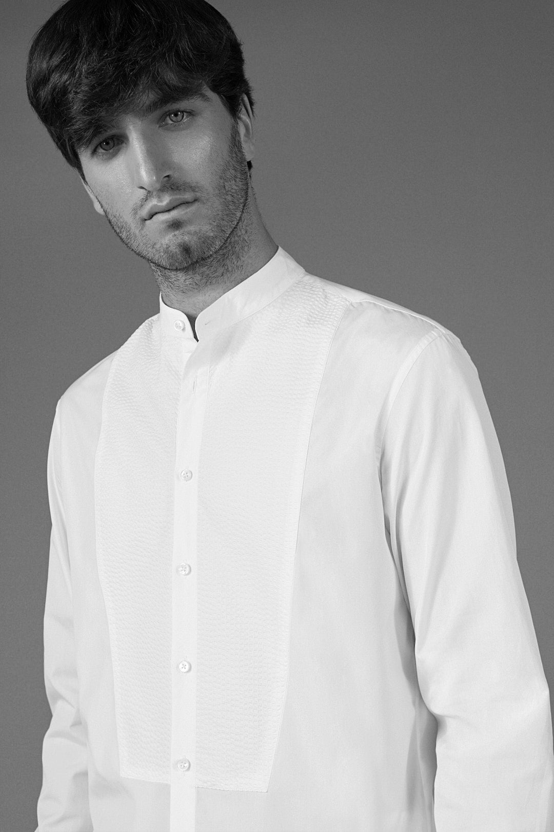 Plan buste d'un homme posant en chemise blanche à plastron texturé en seersucker, avec un col officier.