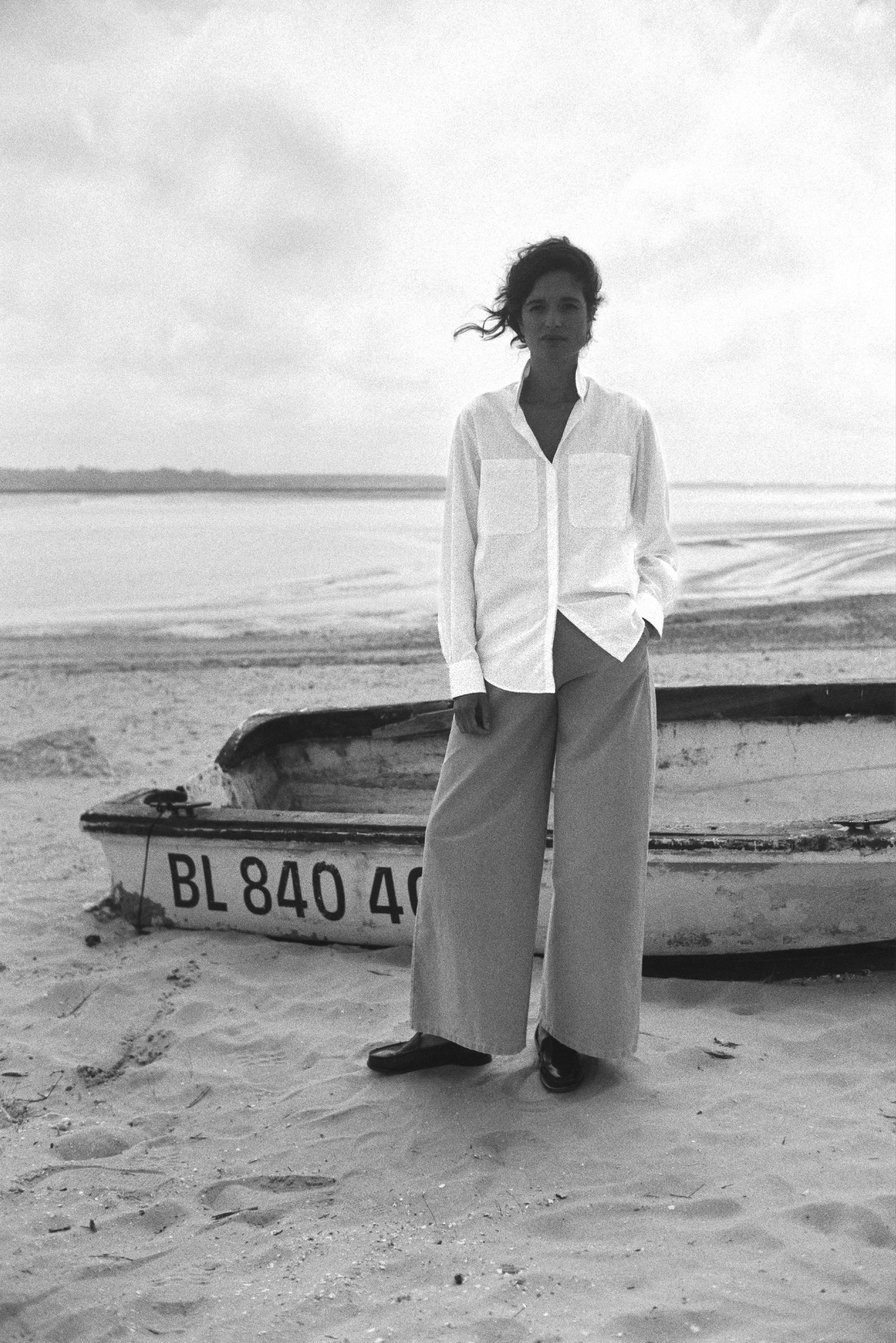 BOURRIENNE PARIS X: Photo vue de face, le mannequin est sur la plage et porte une chemise en coton et à rayures blanches ton sur ton, la photo est en noir et blanc.