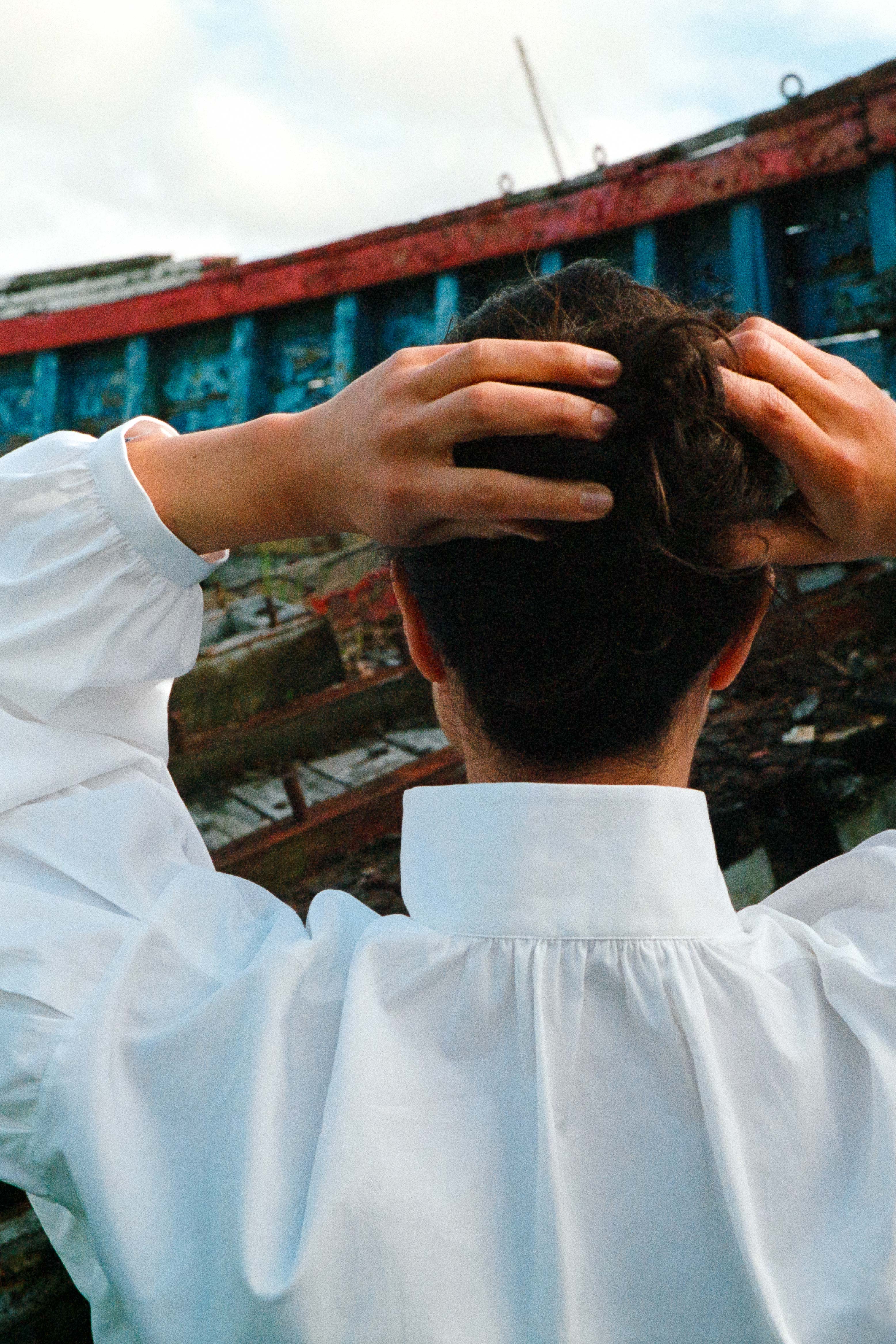 BOURRIENNE PARIS X: Photo prise de dos, et close up sur les détails du col ainsi que des manches. Le mannequin se touche les cheveux ce qui nous permet de mieux voir les manches napoléoniennes bouffantes. Le col de cette chemise est haut.