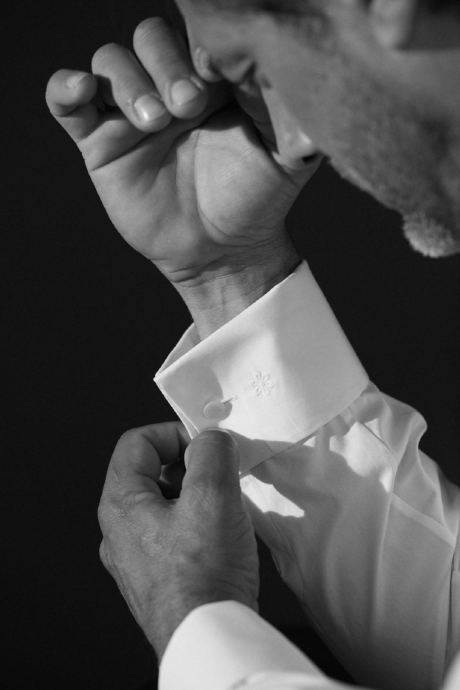 Photo serré d'un homme de profil qui porte une chemise blanche. On aperçoit légèrement  son visage de profil en troisième plan, on voit en premier plan sa main gauche qui pince le poignet mousquetaire de son bras droit en deuxième plan. 