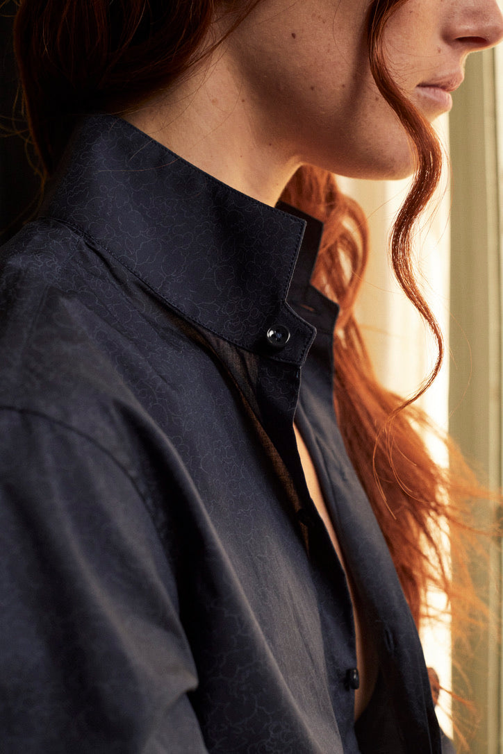 Photo plan poitrine d'une femme rousse de profil qui porte une chemise AMAZONE bleu marine imprimé liberty Bourrienne Paris X. La chemise est déboutonnée, ce qui forme un décolleté en V, on aperçoit de près le col ancien de la chemise qui est relevé, lui revisite le vestiaire homme. 