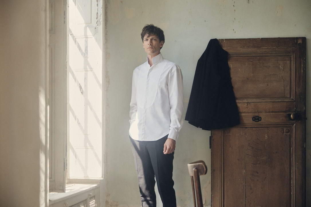 Photo plan américain d'un homme debout portant une chemise blanche, avec des poignets Français, une chemise à la coupe Bourrienne, un col haut officier avec un plastron. 