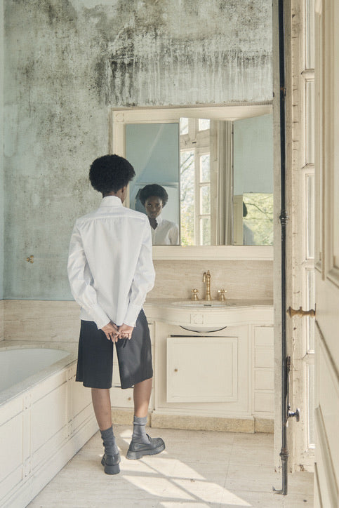 Femme de dos dans une salle de bain, vêtue d'une chemise blanche Bourrienne Paris X.