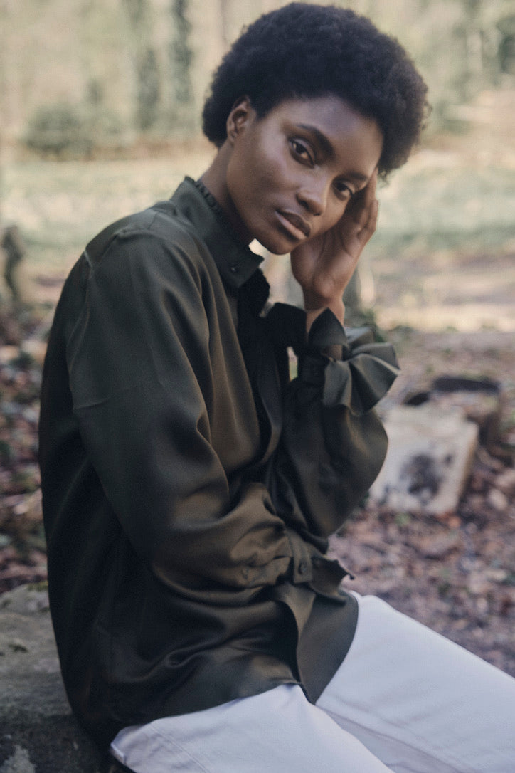 Chemise BOUDOIR Soie couleur Kaki portée par une mannequin assise de profil.