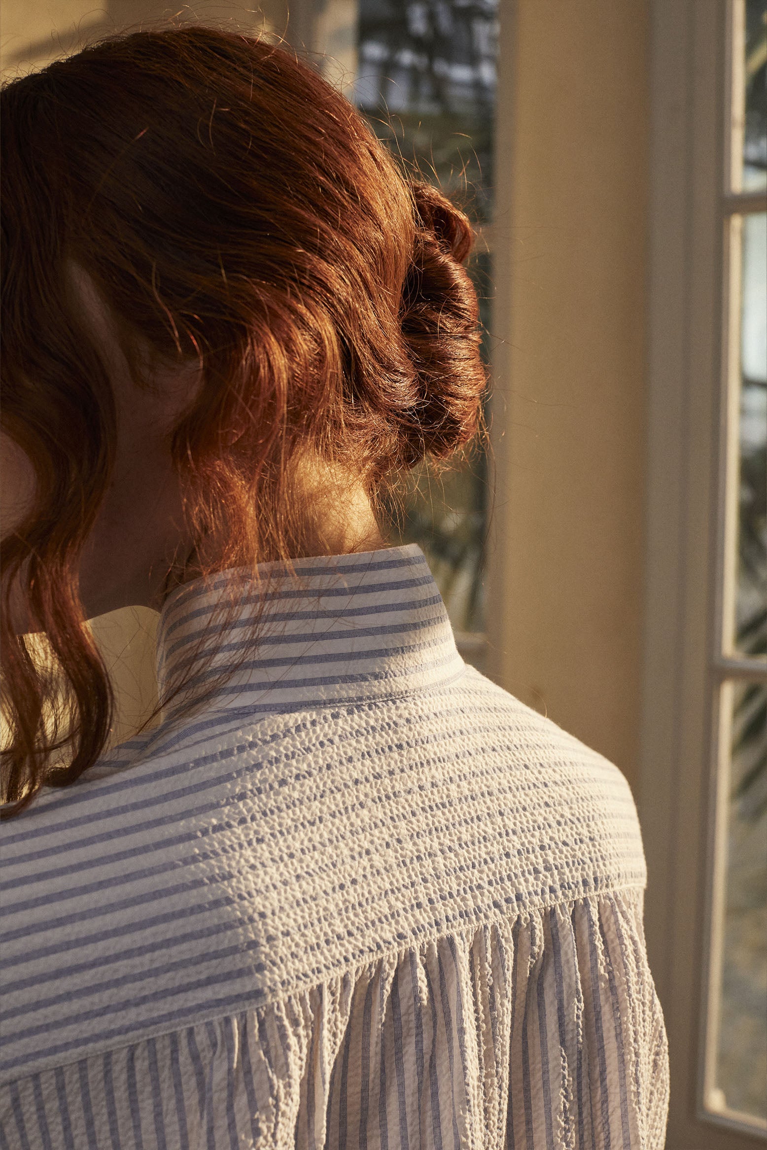 Chemise AMAZONE Rayée bleu et blanc vue de dos, portée par une mannequin rousse. On distingue les fronces dans le dos et le col haut, détails caractéristiques de Bourrienne Paris X.