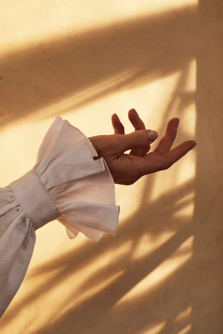 Photo close-up d'un poignet de chemise blanche à volants. La chemise se nomme BOUDOIR elle est en LIN Blanc aérien et léger avec des manches légèrement bouffantes ornées de volants, qui tombent avec élégance sur la main. 