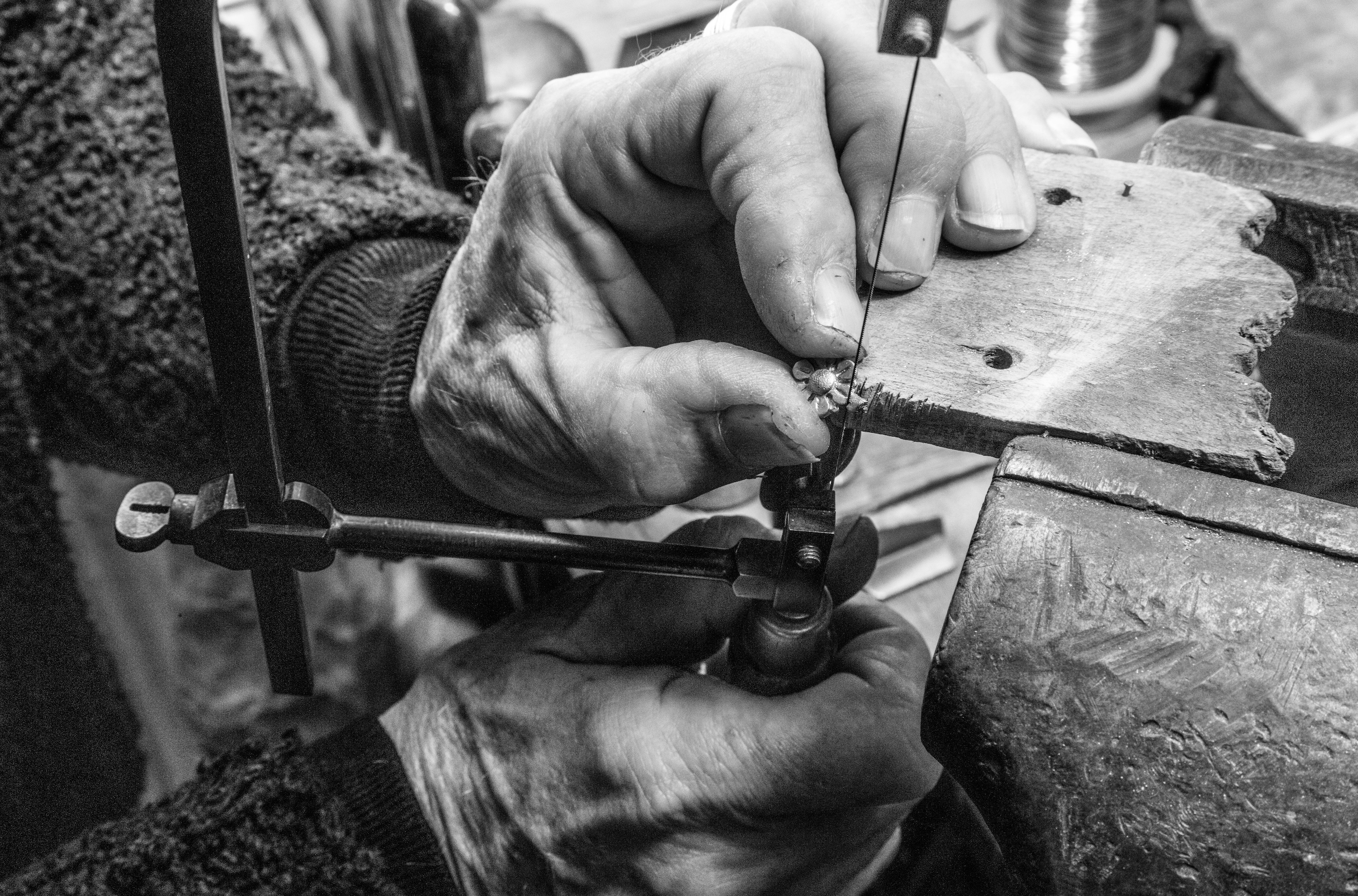 Mains d'artisan en train de façonner une fleur en métal, qui représente la fleur de Bourrienne. l'une des deux mainstient fermement le socle, la seconde tient la fleur afin de la découper dans le métal.