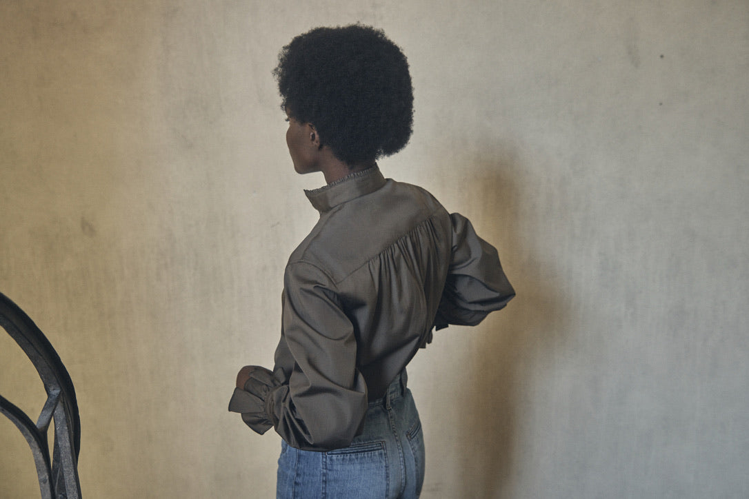 Femme portant la chemise BOUDOIR Kaki, de dos dans les escaliers. On distingue les délicates fronces dans le dos de la chemise.