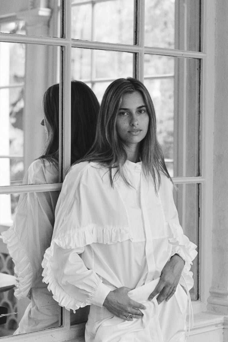 Femme adossée contre un miroir portant la chemise DRAMA.