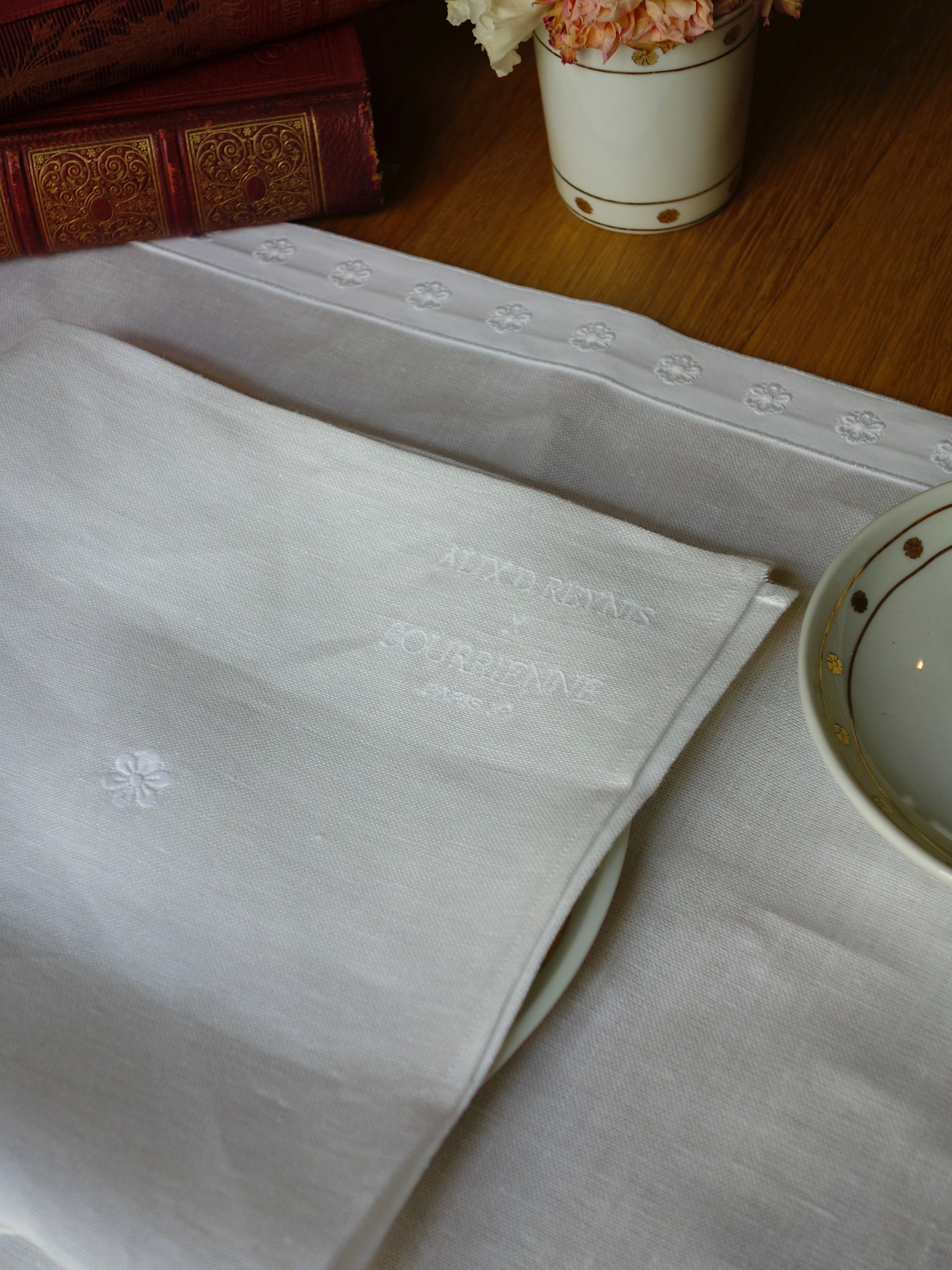 serviette en lin blanche brodée sur set de table au galon brodé, posés
 sur une table en bois