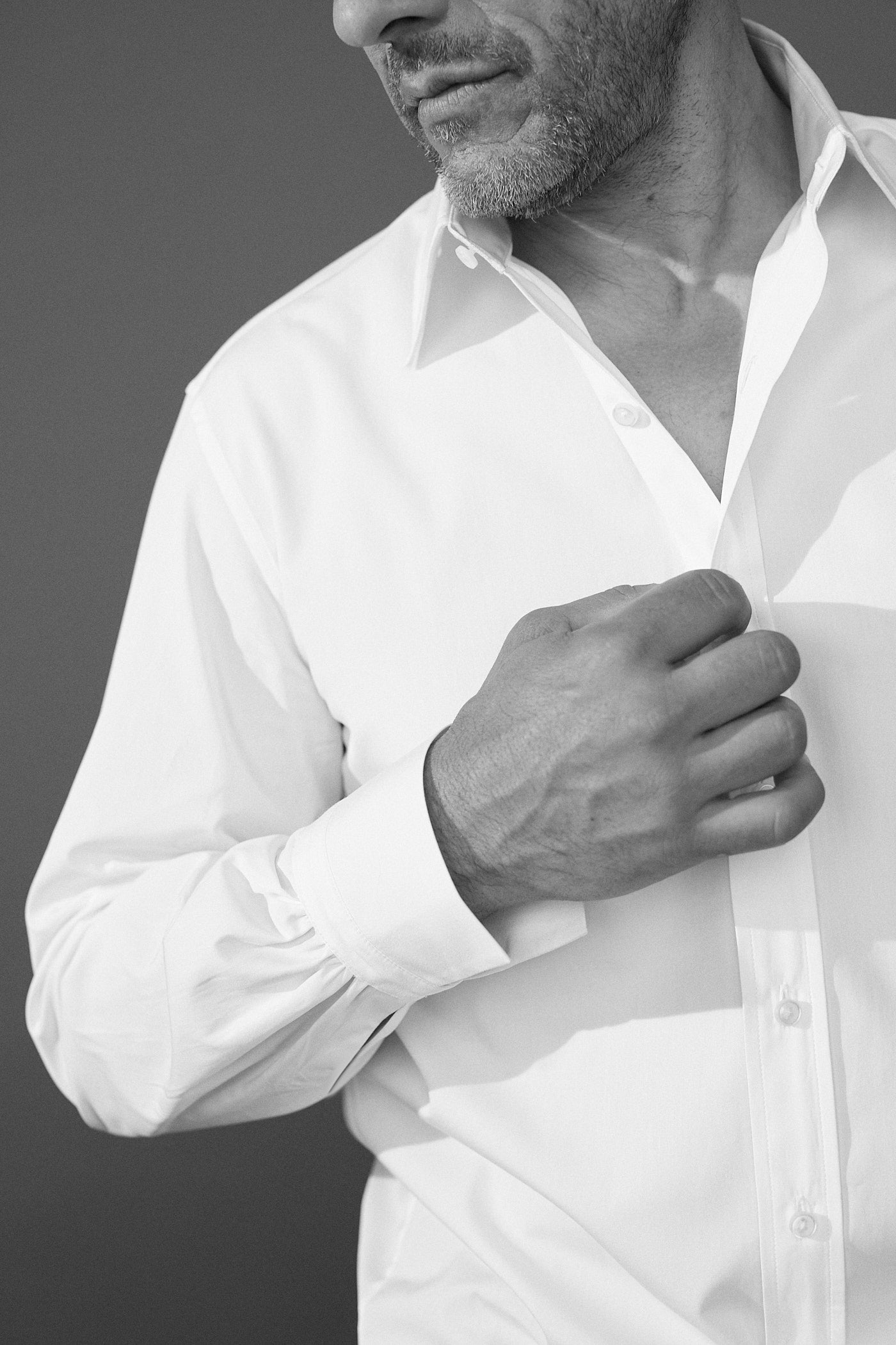 Photo noir et blanc plan serré d'un homme portant une chemise en popeline blanche double retors, col français et poignets bourrienne. On voit les details du poignet de la chemise avec les fronces. On ne voit que le bas de son visage, la photo s'arrête à son nez. 