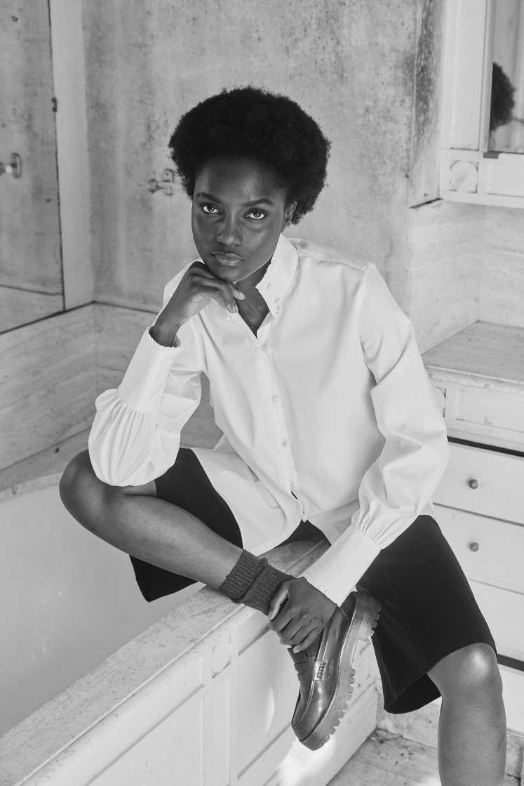 Femme assise sur une baignoire, portant la chemise PRÉCIEUSE, avec un col haut et des poignets allongés, coupe ajustée.