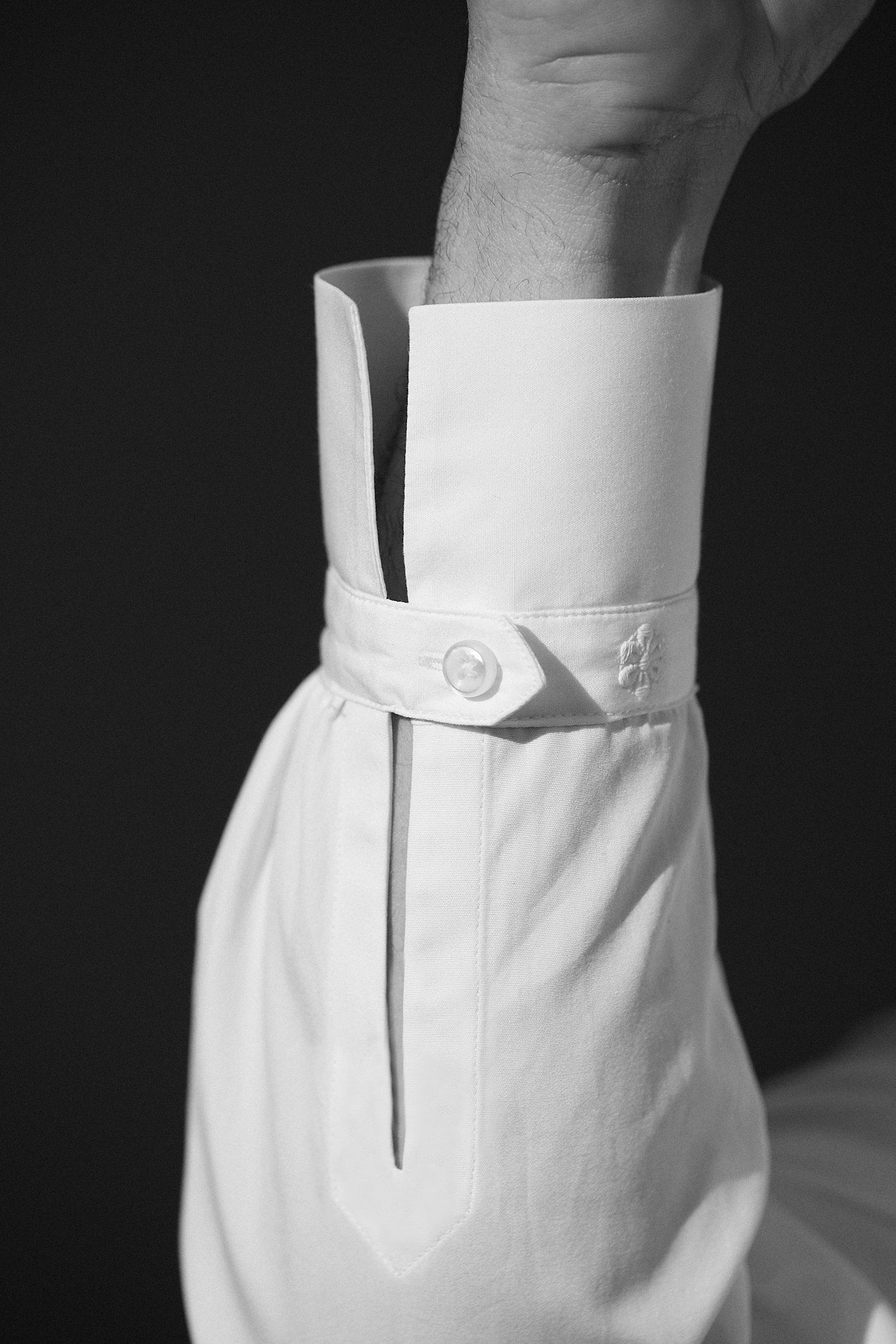 Photo noir et blanc plan serré d'un poignet d'un homme portant une chemise en popeline blanche double retors, col français et poignets bourrienne. On aperçoit visiblement le detail du poignet avec le bouton. 