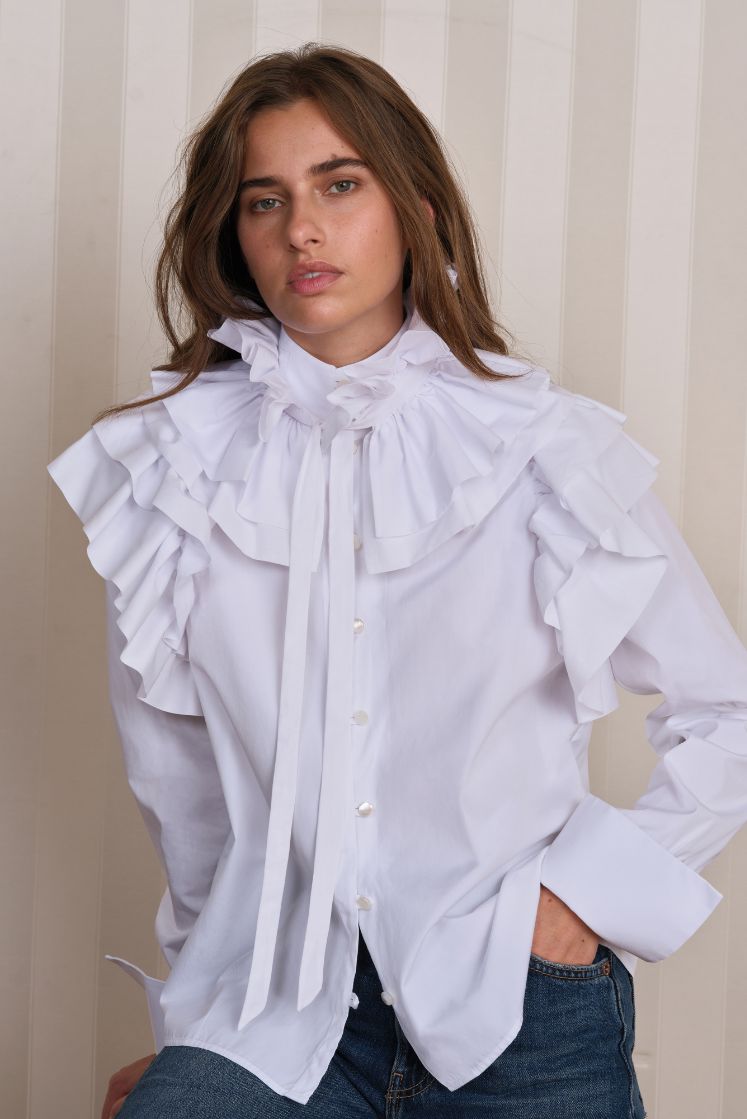 Femme portant la chemise FORTUNÉE avec des volants sur les épaules et le col à volants amovible noué autour du cou. 