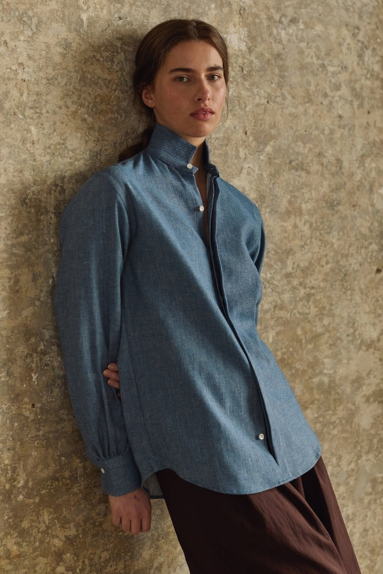 femme adossée contre un mur portant la chemise amazone en denim bleu clair