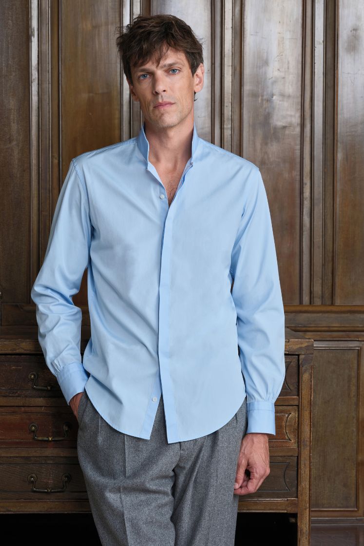 Homme portant la chemise APPARAT en popeline de coton bleu ciel à col haut associée à un pantalon gris. 