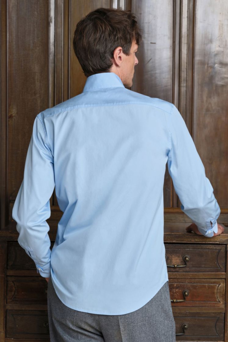 Homme de dos portant la chemise APPARAT en popeline de coton bleu ciel à col haut, coupe ajustée. 