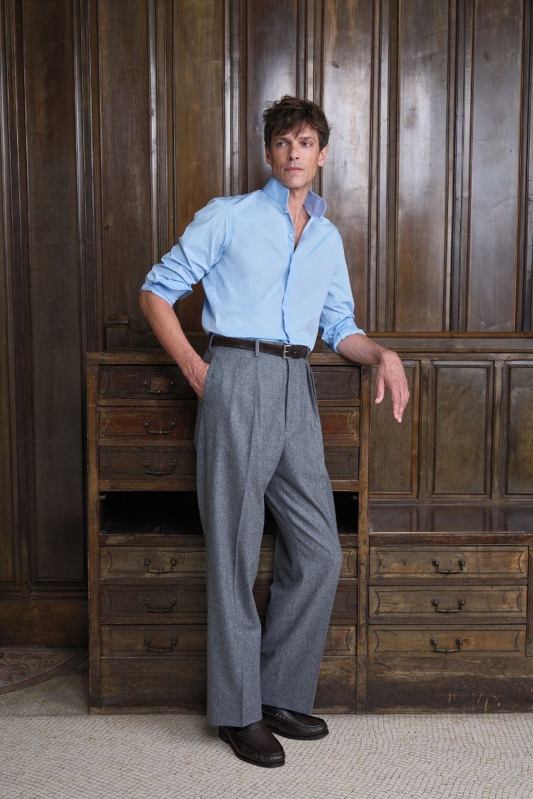 Homme portant la chemise APPARAT en popeline de coton bleu ciel à col haut, associée à un pantalon gris et des mocassins noirs. 