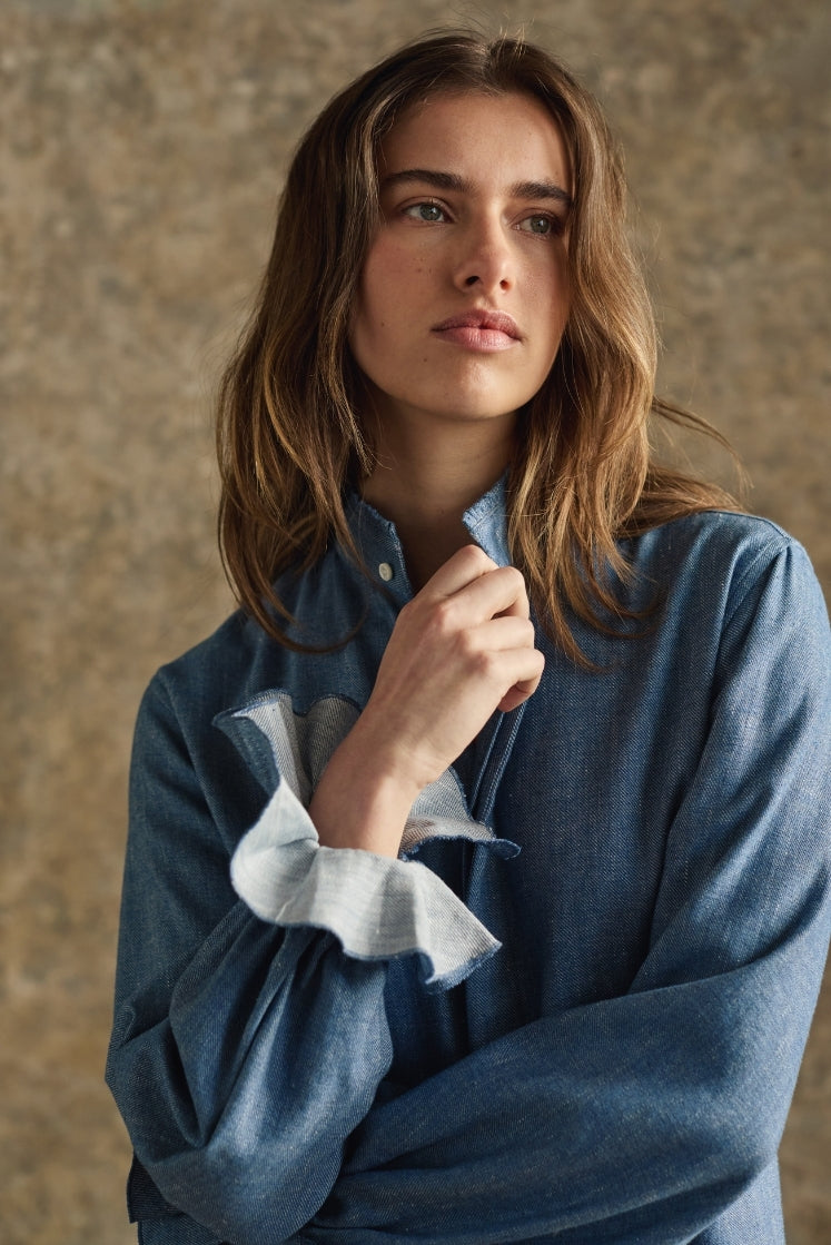 Femme portant une chemise en denim bleu clair avec col et poignets à volants, détails artisanaux, luxe français