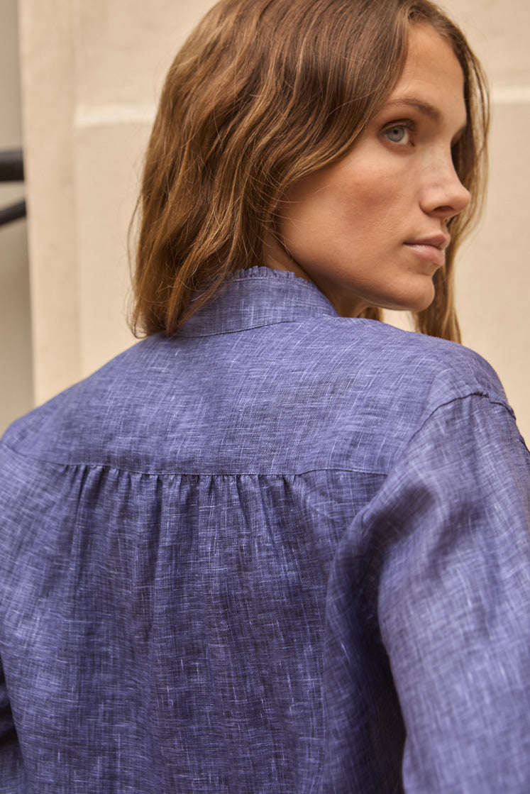 Femme portant une chemise en lin bleu de dos, on distingue les délicates fronces de la chemise dans le dos pour donner du volume.