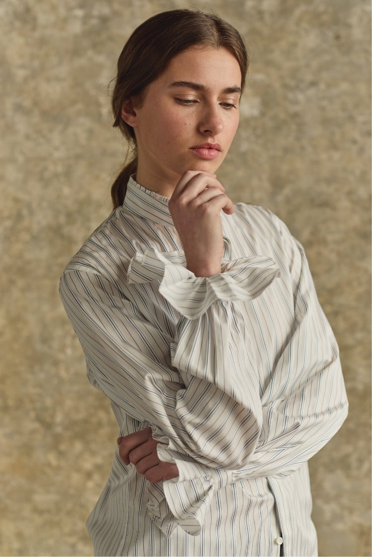 Femme portant chemise BOUDOIR rayée bleu gris, col froufrou, pose élégante et contemplative