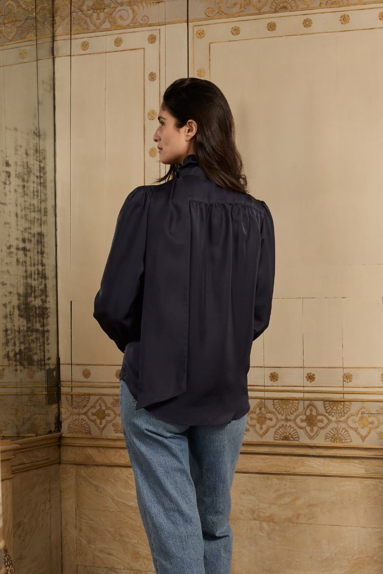 Femme de dos portant la chemise COMTESSE en soie bleu marine marquée par une série de fronces dans le dos.