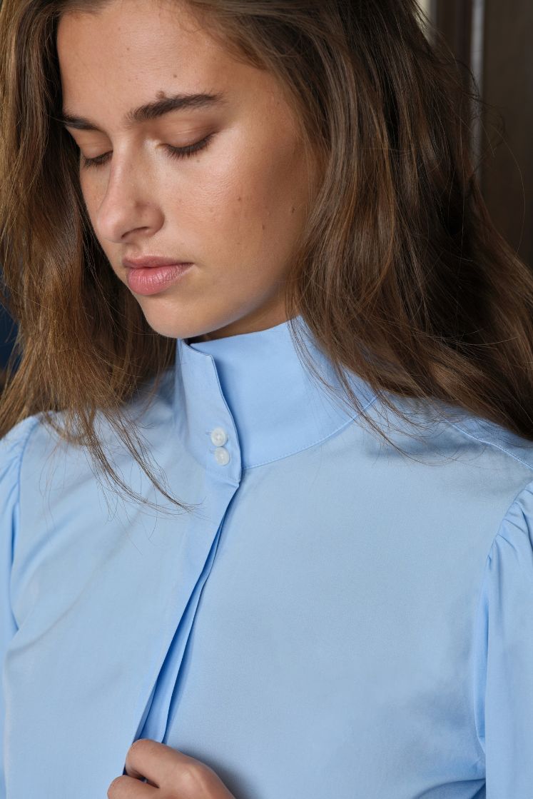 Femme portant une chemise bleu ciel à col haut boutonné. 