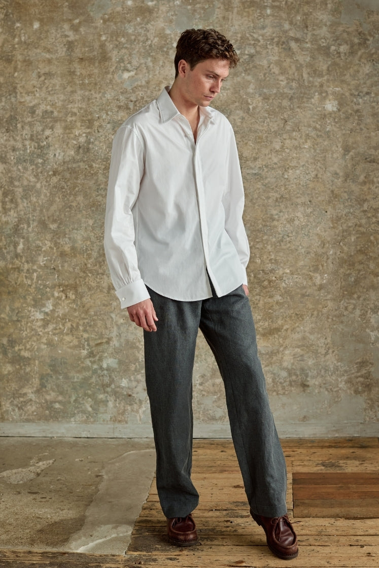 Homme portant la chemise blanche GALERIE en popeline de coton italienne double retors, col français et poignets mousquetaires, sublimée par un passepoil blanc en finition, plan plein pied. 