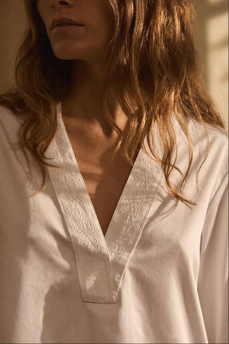Closeup sur le col V d'une blouse blanche avec un galon brodé.