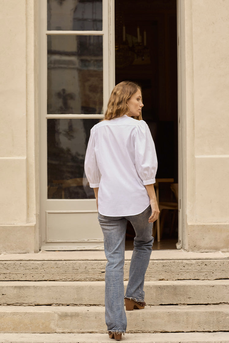 Femme montant les escaliers de dos portant la chemise REVERIE à manches bouffantes coupées 3/4.
