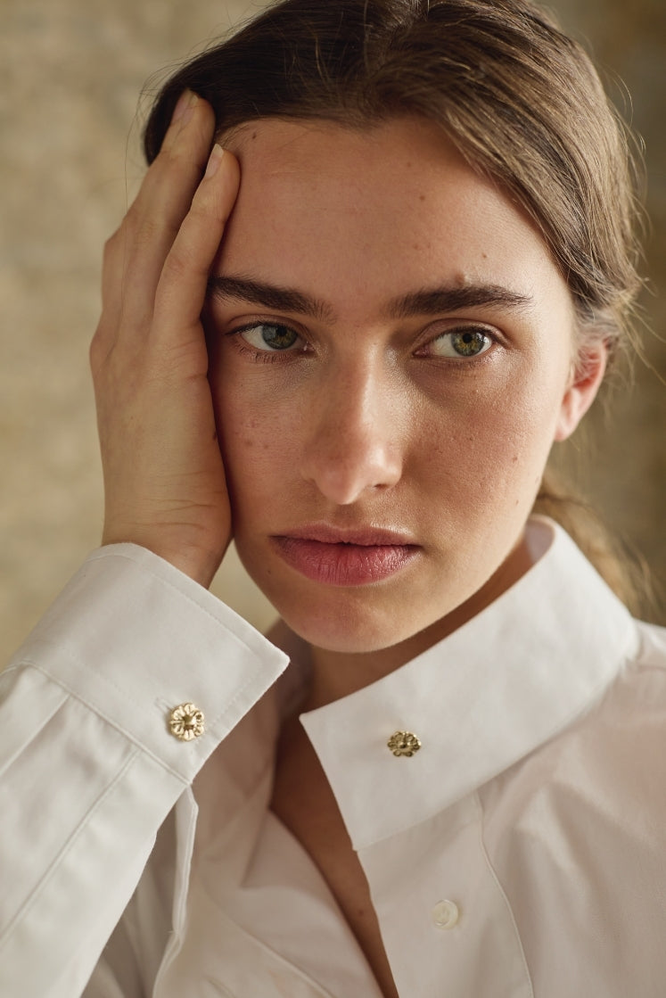 Femme portant une chemise blanche avec boutons dorés reprenant la Fleur de l'Hôtel de Bourrienne