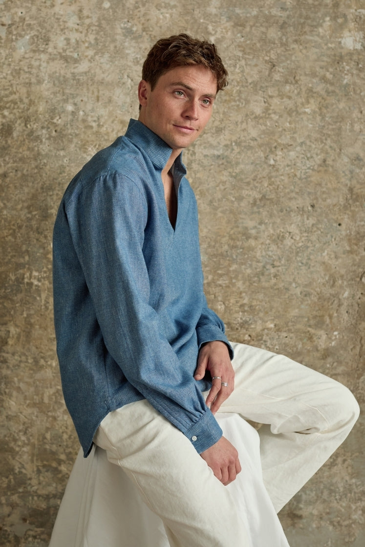 Homme portant la chemise SCULPTEUR en denim bleu clair assis sur un tabouret haut de profil. 